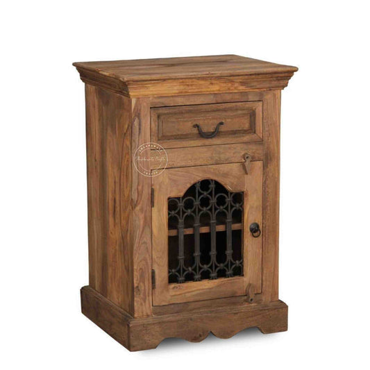 A wooden bedside table with a drawer, a shelf, natural finish and an iron jali door in a white background.
