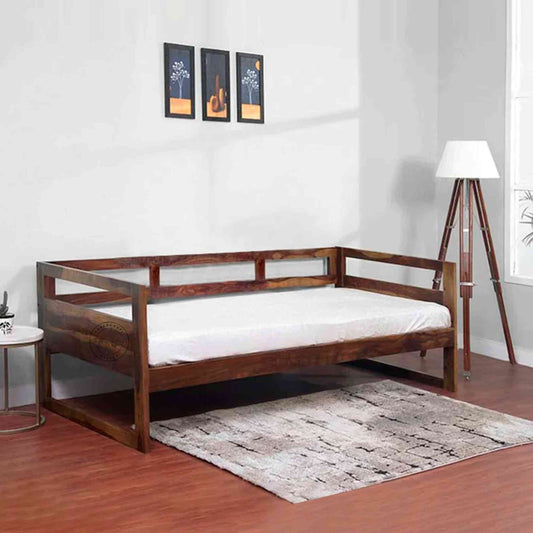 A foldable wooden daybed made of Sheesham wood, with a white cushion, sits in a room with minimalist decor.