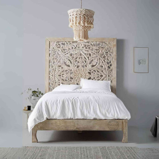 A king-size wooden bed with hand carvings on the headboard, painted in a rustic white finish.