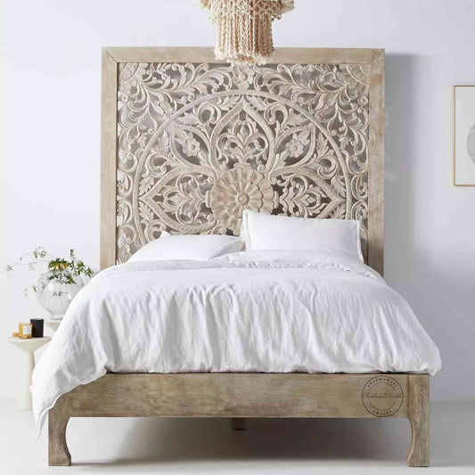 A king-size wooden bed with hand carvings on the headboard, painted in a rustic white finish.