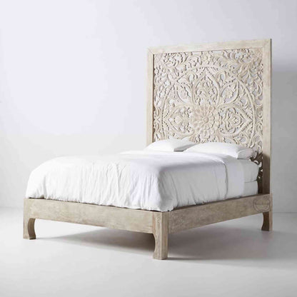 Side view of a king-size wooden bed with hand carvings on the headboard, painted in a rustic white finish.