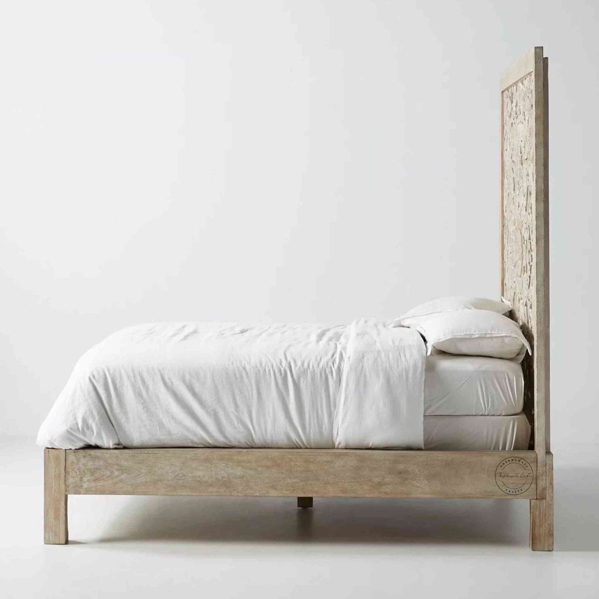 Side view of a king-size wooden bed with hand carvings on the headboard, painted in a rustic white finish.