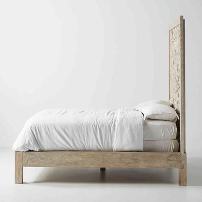 Side view of a king-size wooden bed with hand carvings on the headboard, painted in a rustic white finish.
