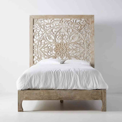 A king-size wooden bed with hand carvings on the headboard, painted in a rustic white finish.