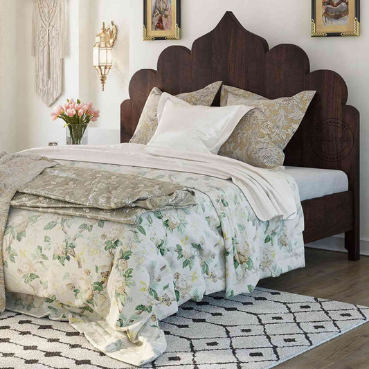 A king size Brassico bed made of Sheesham wood with a walnut finish, featuring a floral bedsheet and positioned against a wall.
