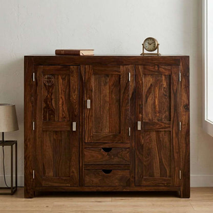 A dark brown wooden cabinet with three doors and two drawers, styled in a minimalist room with a small clock and books on top.
