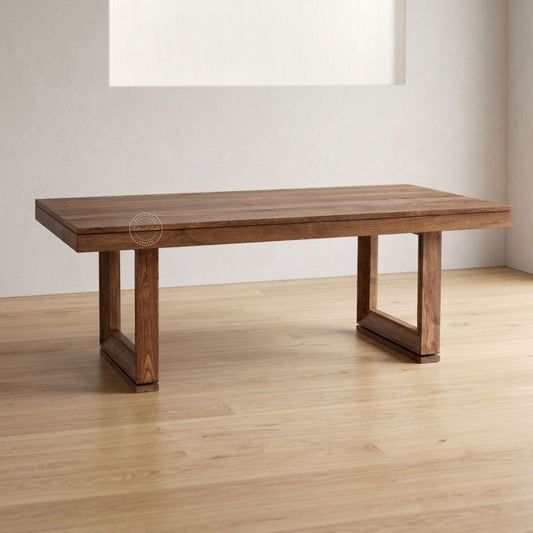 A rectangular wooden dining table with a medium brown finish and a unique open-frame leg design, shown on a light wood floor against a neutral wall.