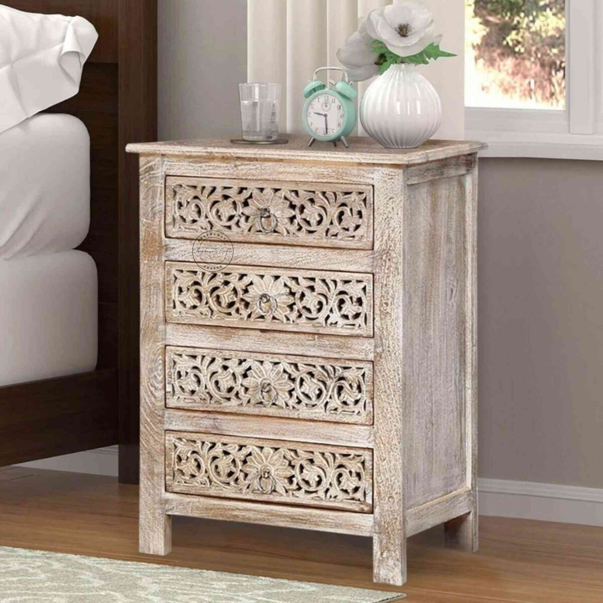 A beige wooden bedside table with four drawers, featuring traditional floral carved designs.