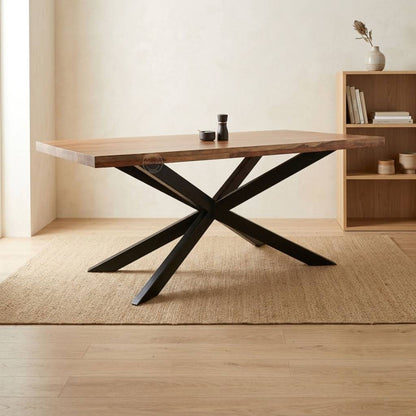 A rustic wooden dining table with a live-edge top and a black metal X-shaped base, styled on a jute rug in a warm, minimalist room.