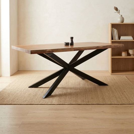 A rustic wooden dining table with a live-edge top and a black metal X-shaped base, styled on a jute rug in a warm, minimalist room.