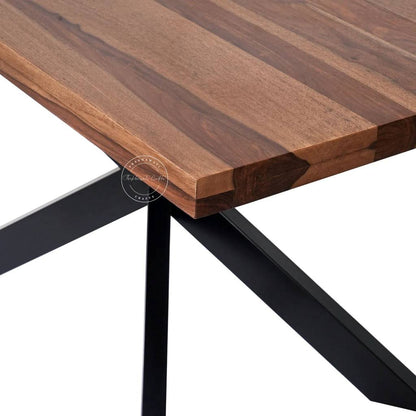 Close-up view of a wooden dining table showing a rich brown wood-grain top and a black metal X-frame base.