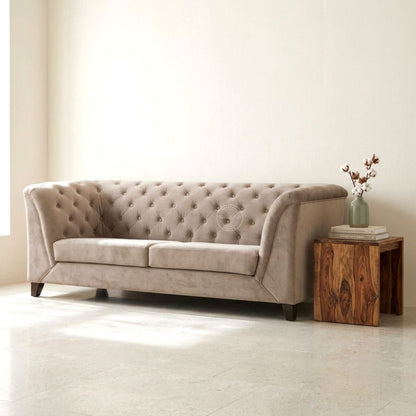 A beige tufted velvet loveseat sofa in a bright, minimalist room, styled with a rustic wooden side table.