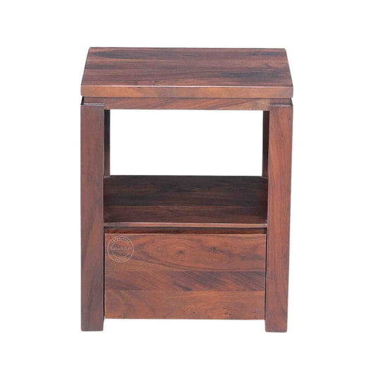 A wooden bedside table made of sheesham wood with a honey finish, featuring a drawer and an open shelf.
