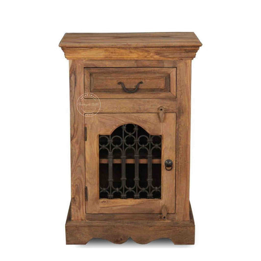 A wooden bedside table with a drawer, a shelf, natural finish and an iron jali door in a white background.