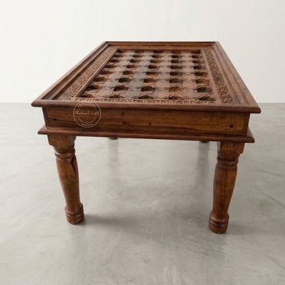 A dark brown carved wooden table with a grid-patterned top and turned legs.