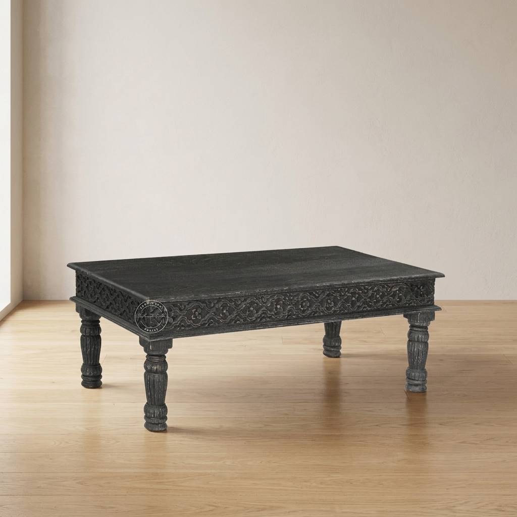 A rectangular, dark-black carved wooden centre table with ornate detailing on the apron and turned legs, set on a light wood floor against a beige wall.