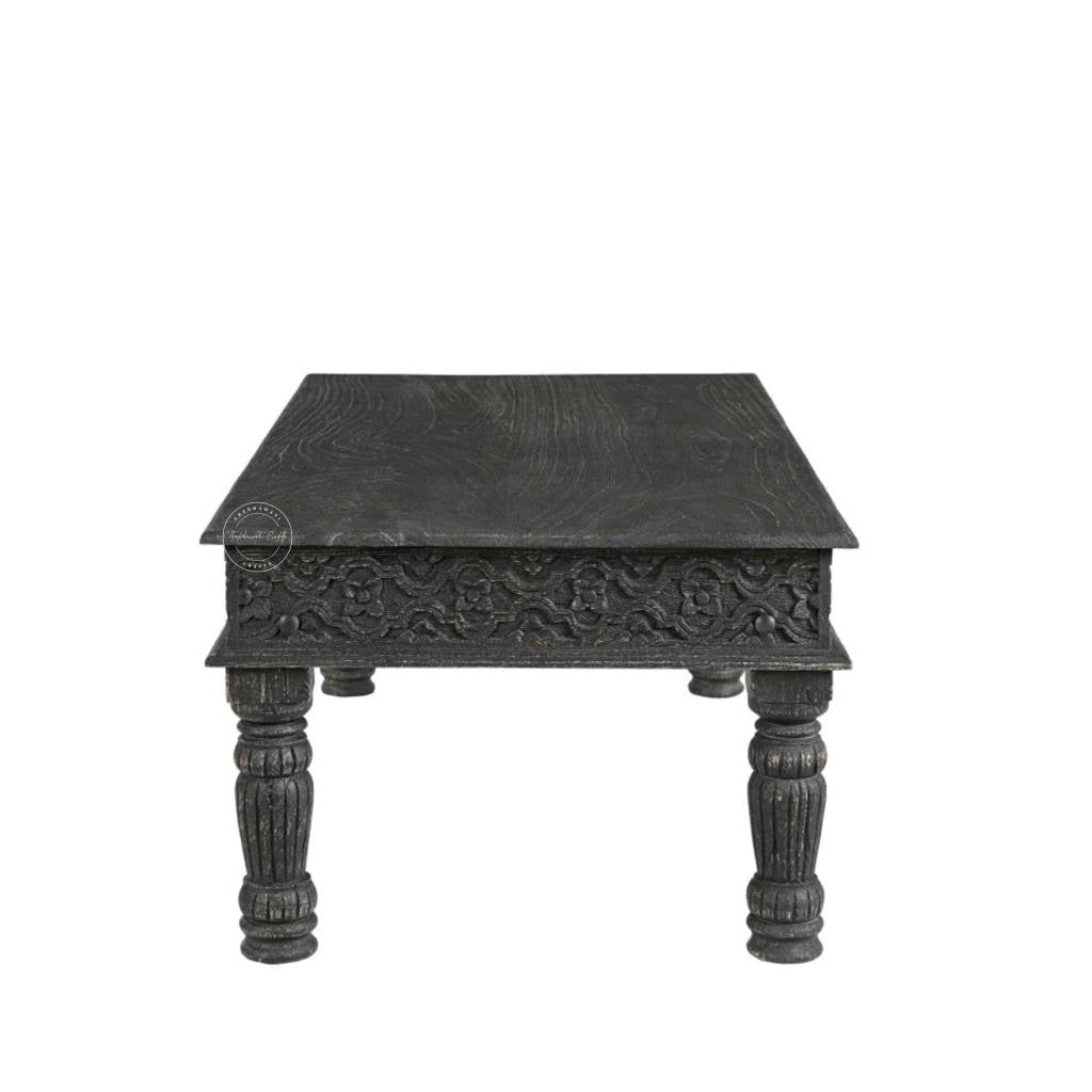 A dark carved wooden table with a square top, ornate floral detailing on the front apron, and four turned legs, shown against a plain white background.