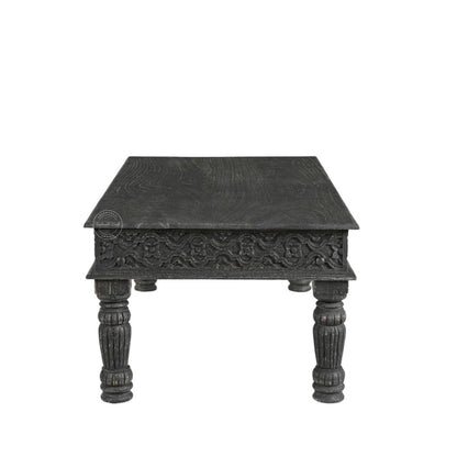 A dark carved wooden table with a square top, ornate floral detailing on the front apron, and four turned legs, shown against a plain white background.